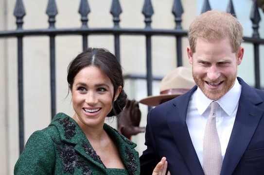 Meghan Markle holds a bouquet of flowers as she wears an emerald dress and coat, next to Prince Harry in a dark suit.