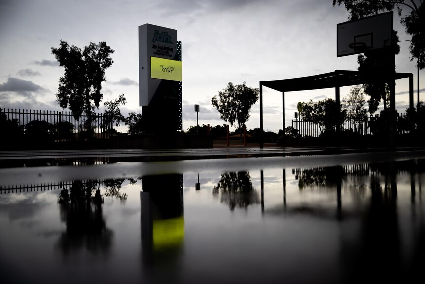 An electronic sign reading yellow alert shines from the bleak landscape of an empty basketball court with rain.