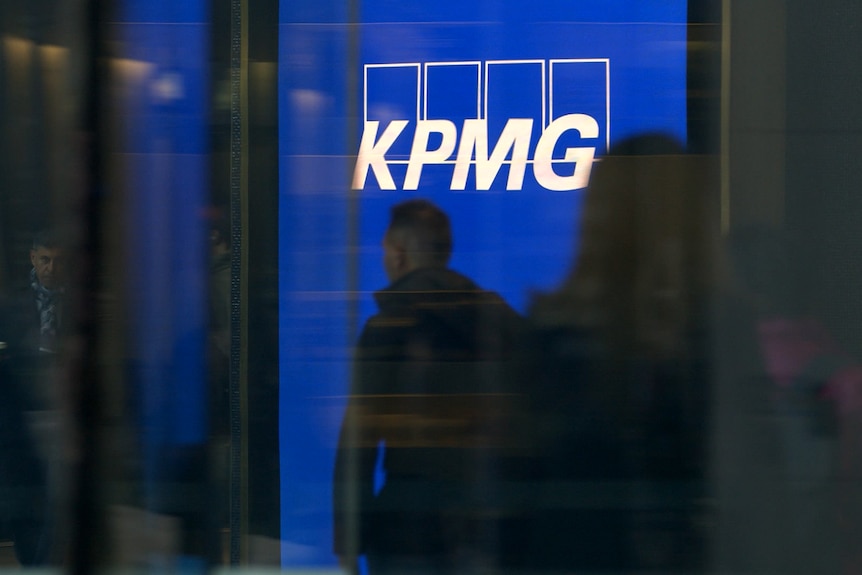 People silhouetted against a white and blue KPMG logo. 