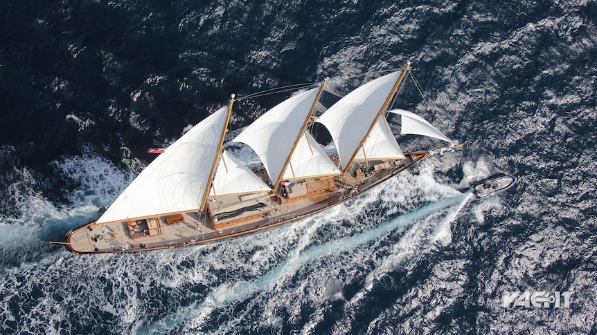 An aerial shot shows a large wooden yacht out at sea, its sails catching the wind