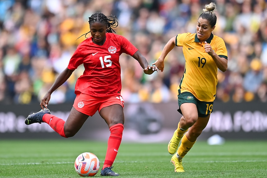 Two women soccer players, one wearing red and the other wearing yellow and green, run during a match