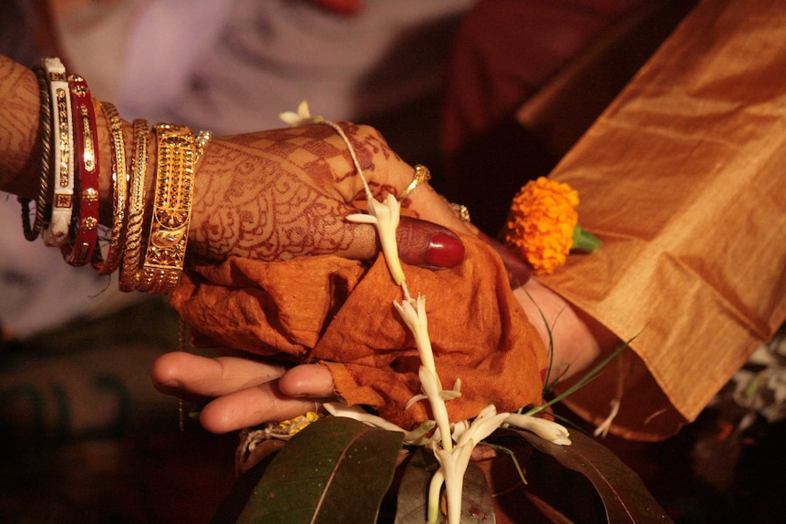A woman's hand, covered in henna and her arm adorned with bangles, rests on top of a man's hand.