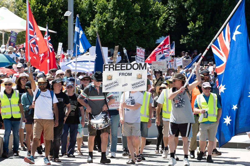 Protesters hold signs saying "freedom from medical apartheid" and "medical tyranny"