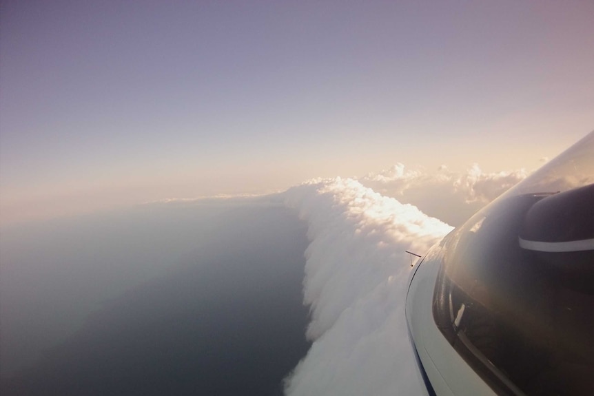 A tubular morning glory cloud extending from behind the front cabin of a glider. Purple skies.