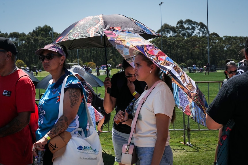 Two women with umbrellas and a woman with a bag around her shoulder in front of them. 