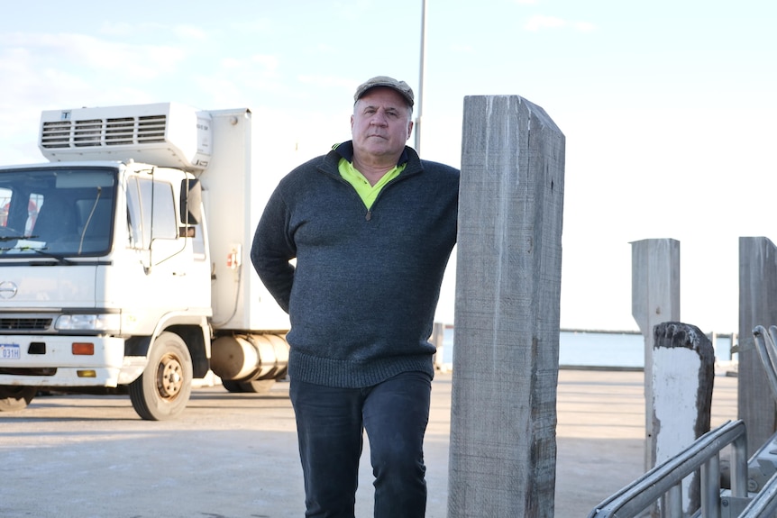 A man looks at the camera as he leans against a jetty pylon.