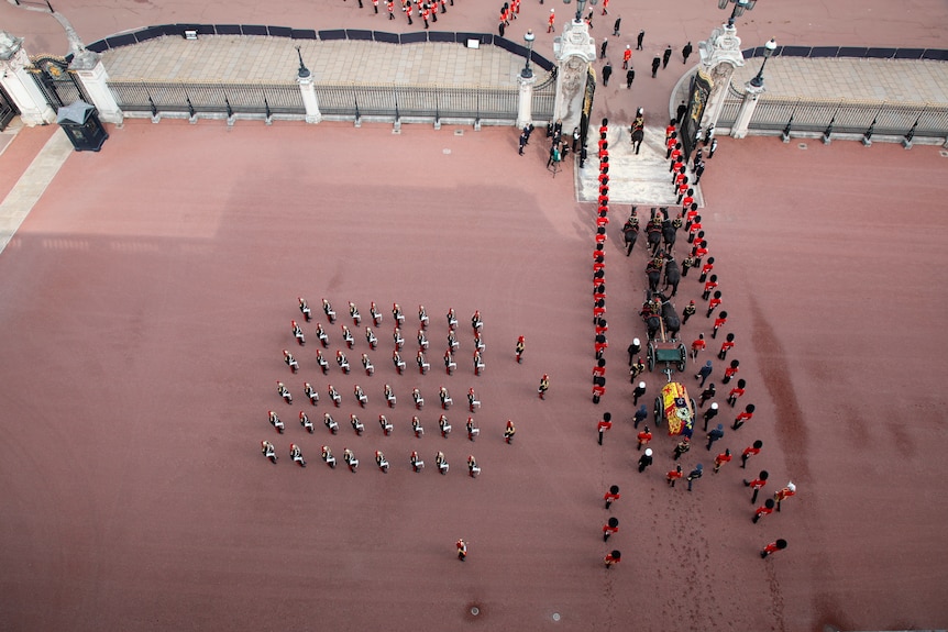 An aerial view of the gates of Buckingham Palace, with eight horses leading out a coffin draped in the Royal Standard