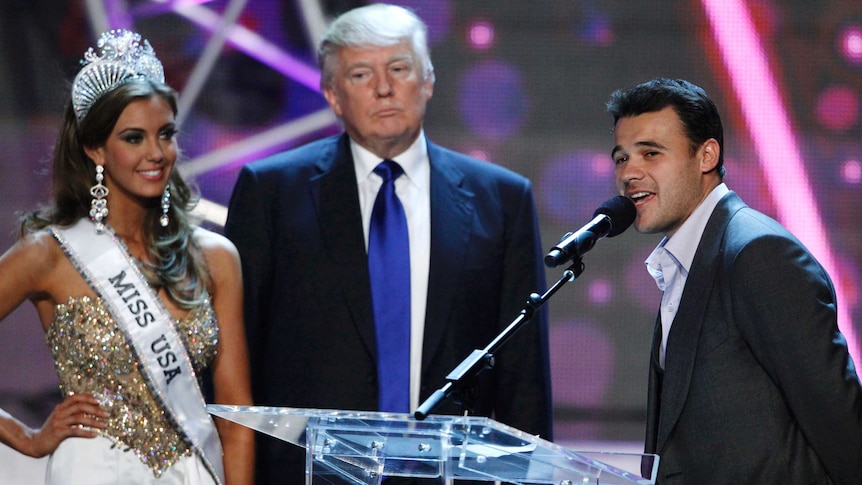 Russian singer Emin Agalarov talks at a podium while Miss USA 2013 Erin Brady and Donald Trump waited behind him.