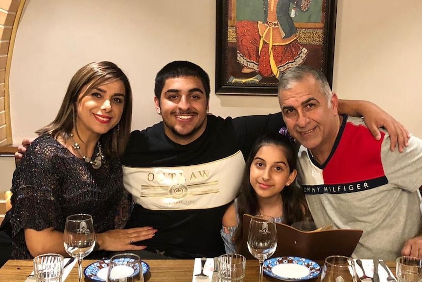 Soori Naeimi Iveli sits smiling next to her husband and children as her son extends his arms around them.