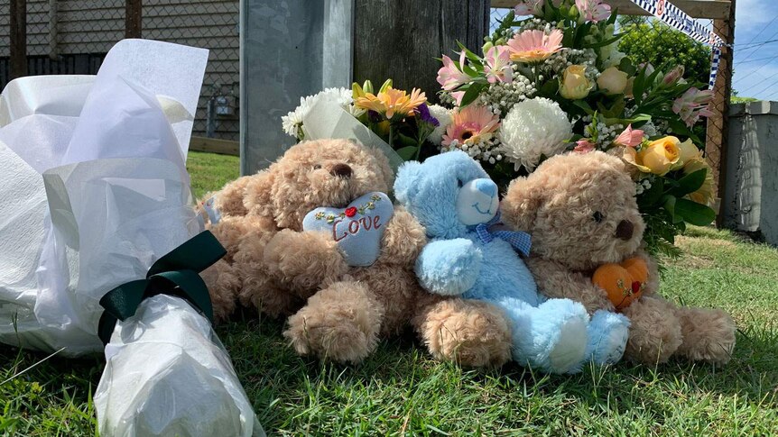 Tributes of toys and flowers in the street where three children died in a car fire.