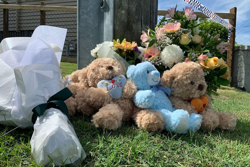 Tributes of toys and flowers in the street where Brisbane man Rowan Baxter and his three children died in a car fire.
