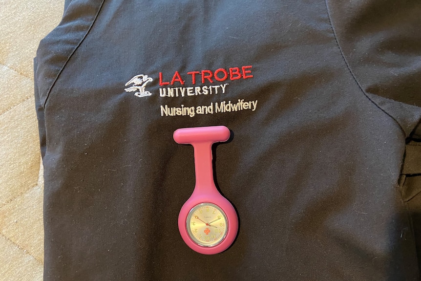 A nurses shirt folded up shows the La Trobe University nursing logo and a timekeeper attached.. 