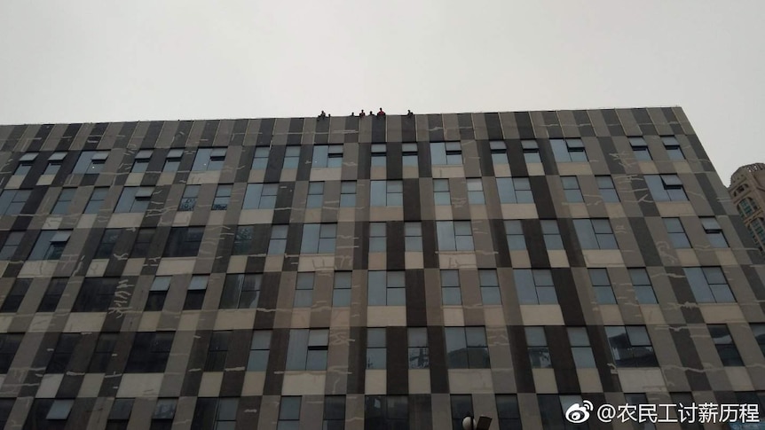 A group of men stand and sit on the roof top of a tall building.
