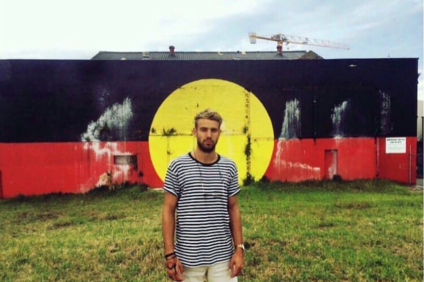 Rulla Kelly-Mansell standing in front of a wall painted like the aboriginal flag