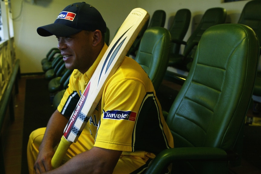 Andrew Symonds, wearing his ODI kit, smiles while sitting and holding his bat