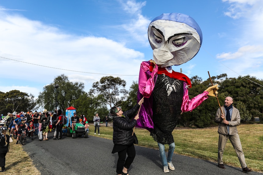 A woman (left) and man (right) hold up an art installation hanging over a performer (centre)