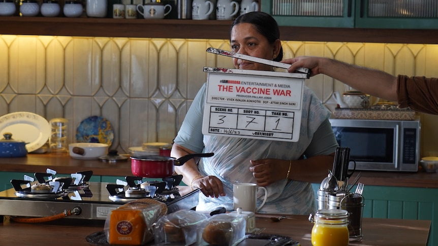 A woman in a kitchen with a film clap board in the foreground.