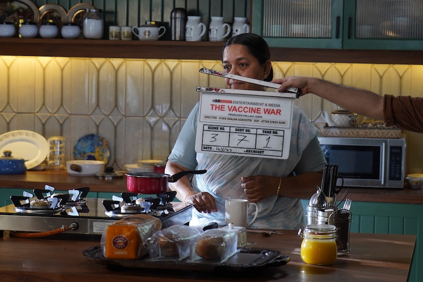 A woman in a kitchen with a film clap board in the foreground.