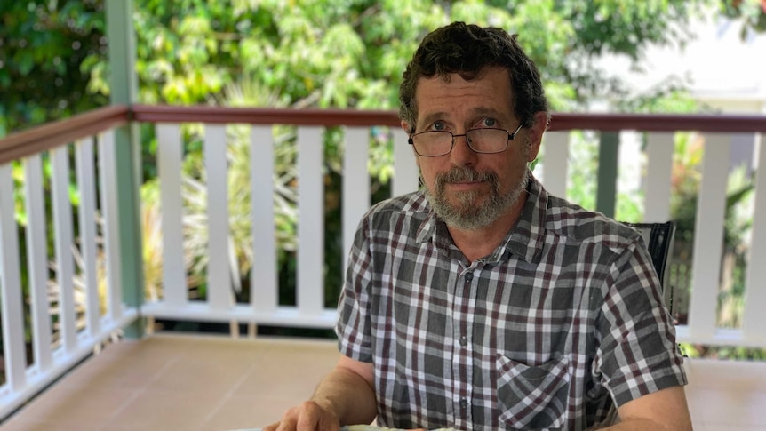 A bearded, bespectacled man of perhaps 50 sitting on a verenda with an earnest expression on his face.