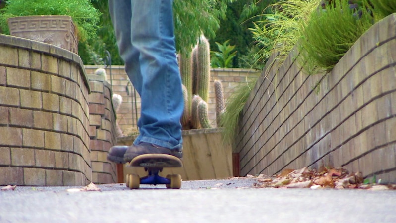 Below knees shot of person on skateboard, skating through walled garden