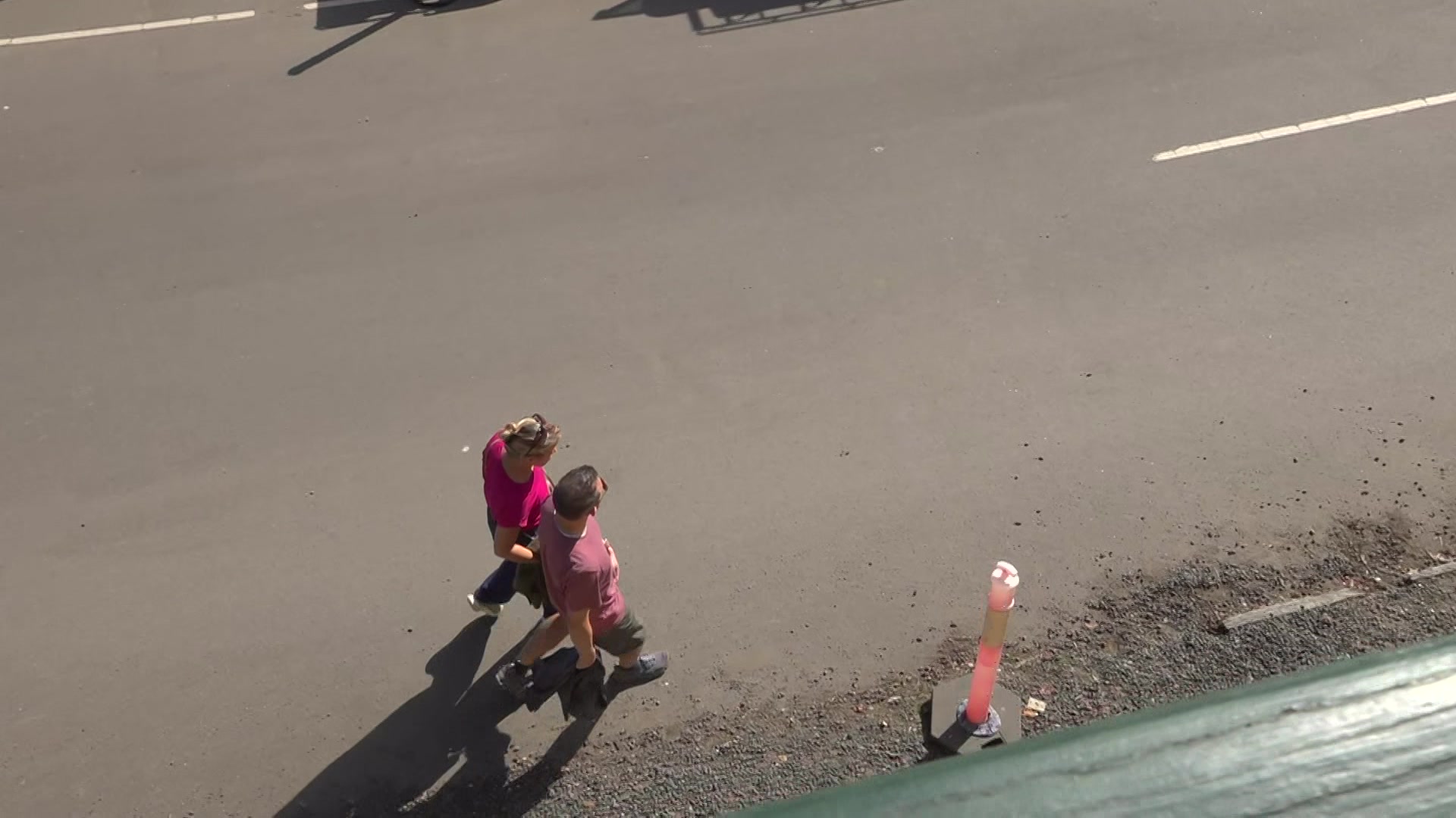 A couple, seen from above, walking on a road around an orange bollard