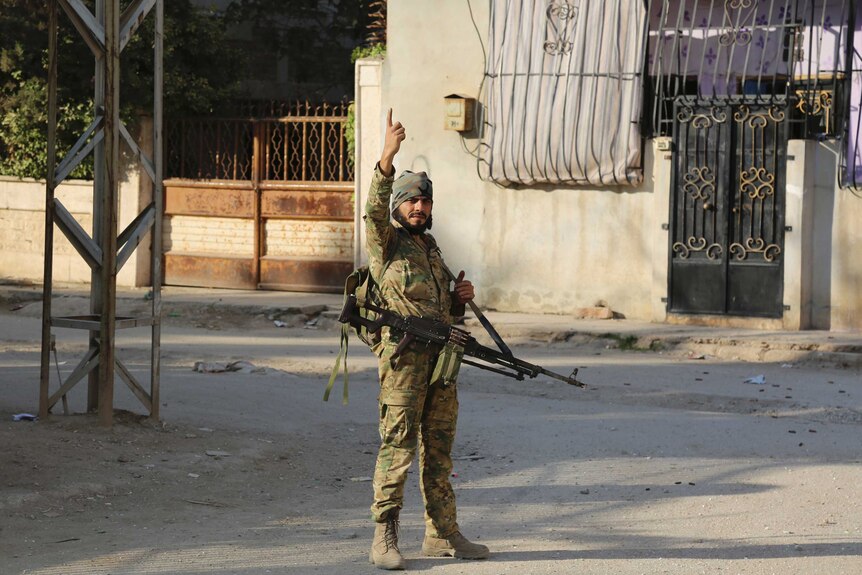 Turkey-backed Syrian fighter in military uniform, gun and hand pointing in the air, stands in an empty Ras al-Yan