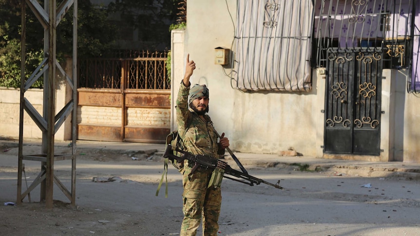 Turkey-backed Syrian fighter in military uniform, gun and hand pointing in the air, stands in an empty Ras al-Yan