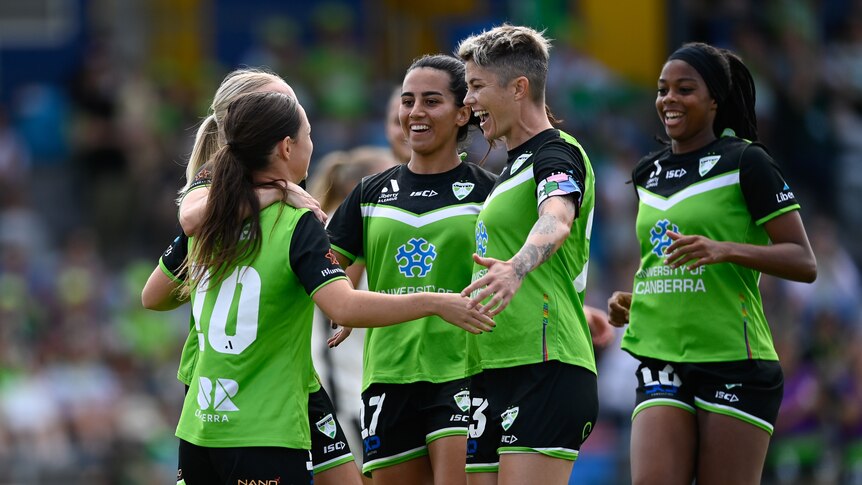Soccer players wearing green, black and white uniforms smile at each other during a game