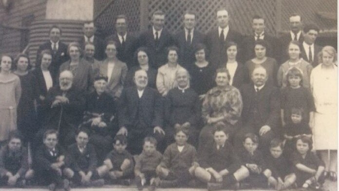 An old photo of a large family with children sitting in the front and adults in the back, most people with serious expressions.