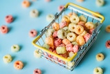 Bright coloured circular breakfast cereal pieces sit in a mini shopping basket.