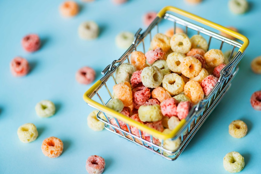 Bright coloured circular breakfast cereal pieces sit in a mini shopping basket.