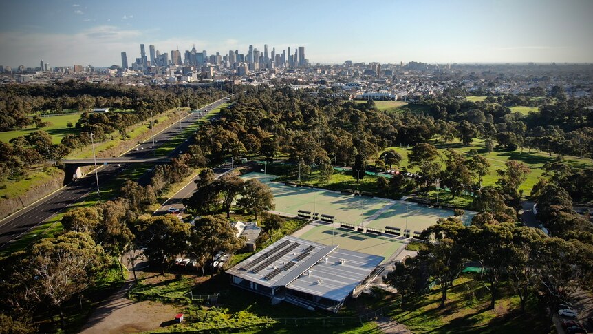 Drone shot of 8 netball courts surrounded by trees, Eastern freeway on left, Melbourne CBD in background