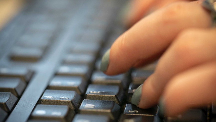 A woman's left hand strikes lettered keys on a computer keyboard with fingers that have painted fingernails.