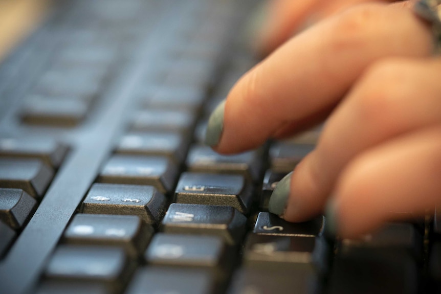 A woman's left hand strikes lettered keys on a computer keyboard with fingers that have painted fingernails.