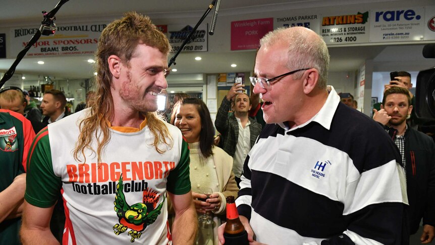 A man with a long red mullet stands next to Prime Minister Scott Morrison at a football club