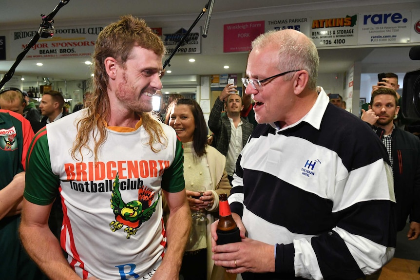 A man with a long red mullet stands next to Prime Minister Scott Morrison at a football club