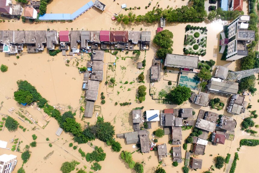 An aerial photo of a village which has been inundated with brown floodwaters.