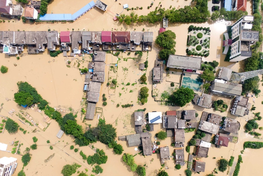 An aerial photo of a village which has been inundated with brown floodwaters.