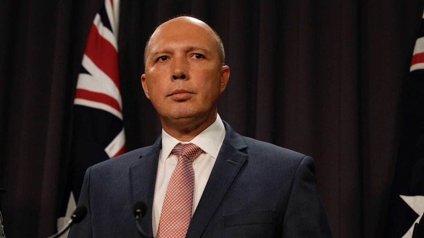 Peter Dutton looks to his left as he stands at a press conference podium with an Australian flag behind him