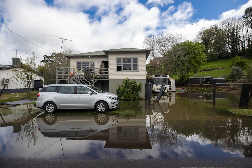 A house with a car out the front has floodwaters up to its front steps.