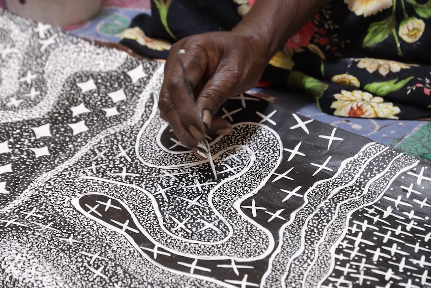 A close-up of Yolŋu artist Naminapu Maymuru-White painting. She is painting a black and white motif on bark.