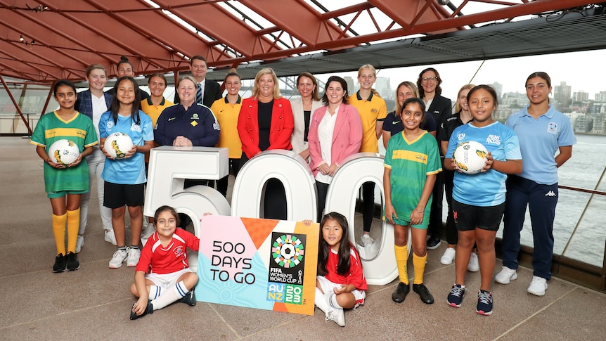 Women and girls stand around a 500 sign holding soccer balls