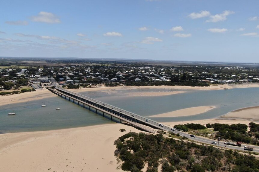 An aerial shot of a bridge linking two towns on the banks of a sandy coastal river.