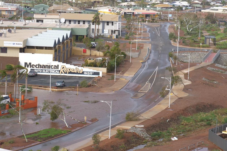 Water fills the road at an intersection with trees lying flat from the wind.