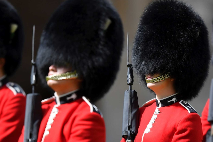 Soldiers in red uniforms and large black furry hats holding rifles