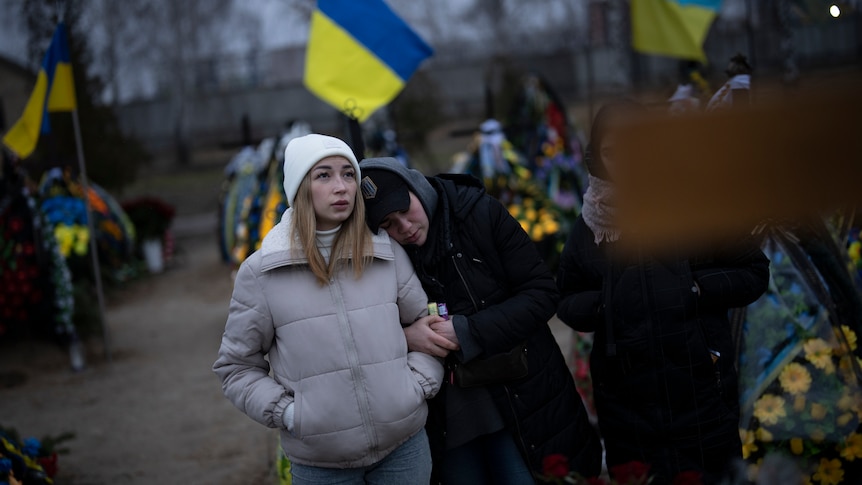 Anastasiia Okhrimenko and Anna Korostenska walk arm in arm through a cemetery