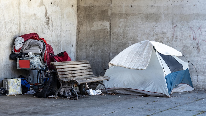 A homeless person's tent next to a pile of possessions on a public street