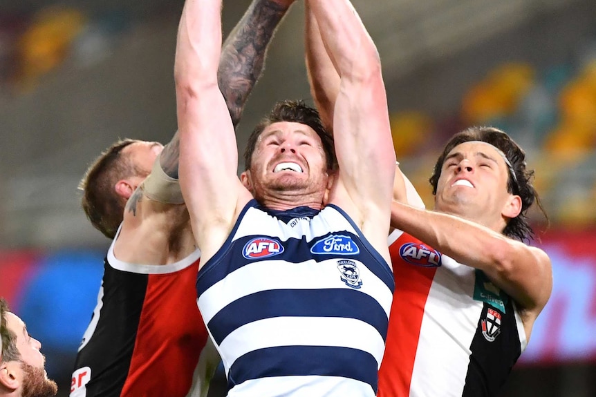 Patrick Dangerfield reaches for a ball above his head, surrounded by two St Kilda opponents who try to punch it away