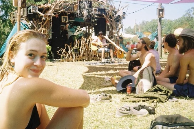 Girl sits on grass in front of a small stage. 