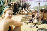 Girl sits on grass in front of a small stage. 